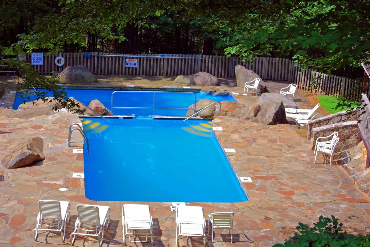 A vibrant exterior image capturing one of the community’s swimming pools, complete with a stone pathway, ample lounge chairs, and natural rock formations. The pool area is surrounded by greenery, evoking a sense of a private resort retreat.