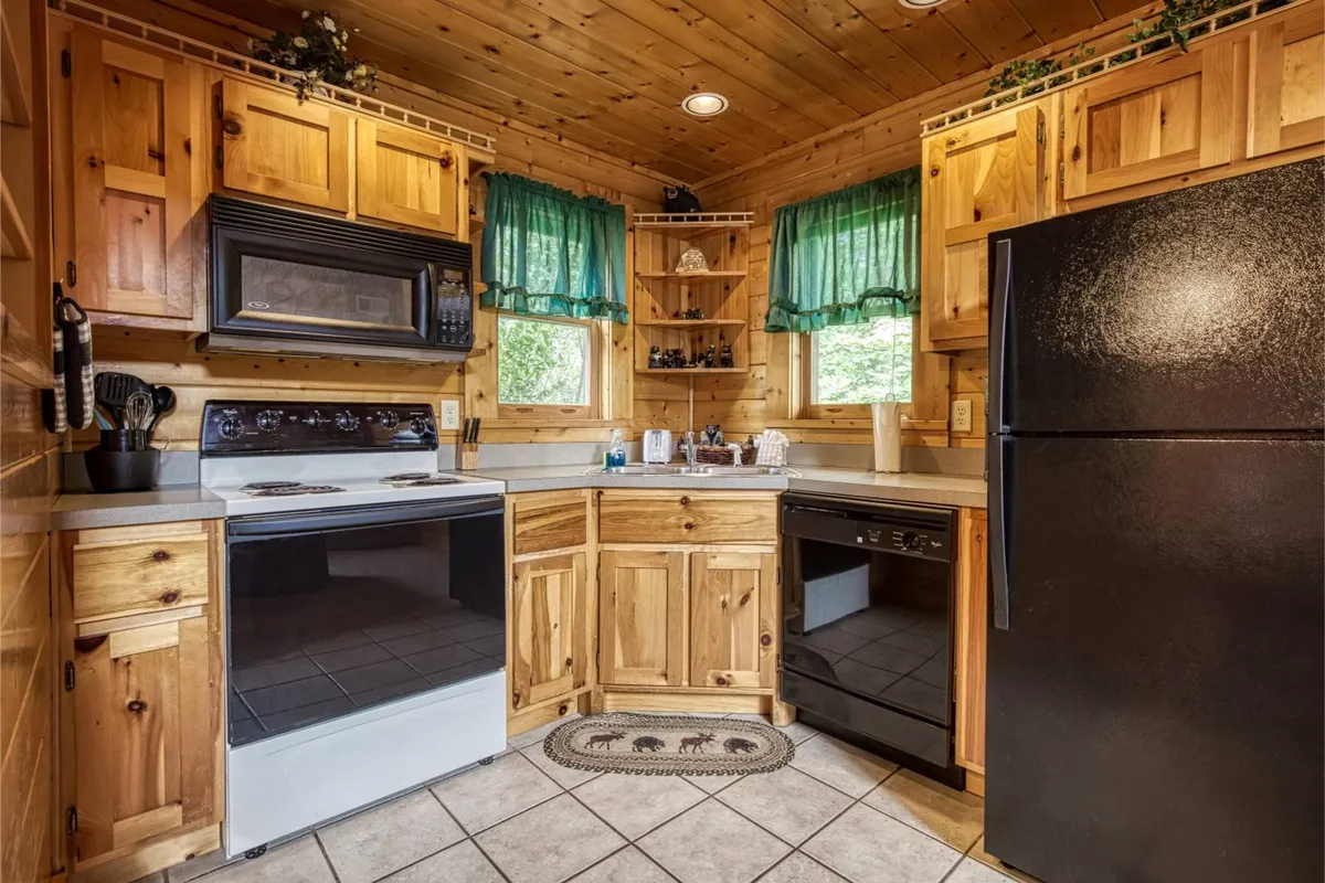 A close-up view of the kitchen showing wooden cabinetry, green curtains, modern kitchen appliances, and tile flooring. The layout and design highlight thoughtful touches ideal for meal preparation and casual family gatherings, reinforcing the idea of a well-appointed and practical chef's nook.