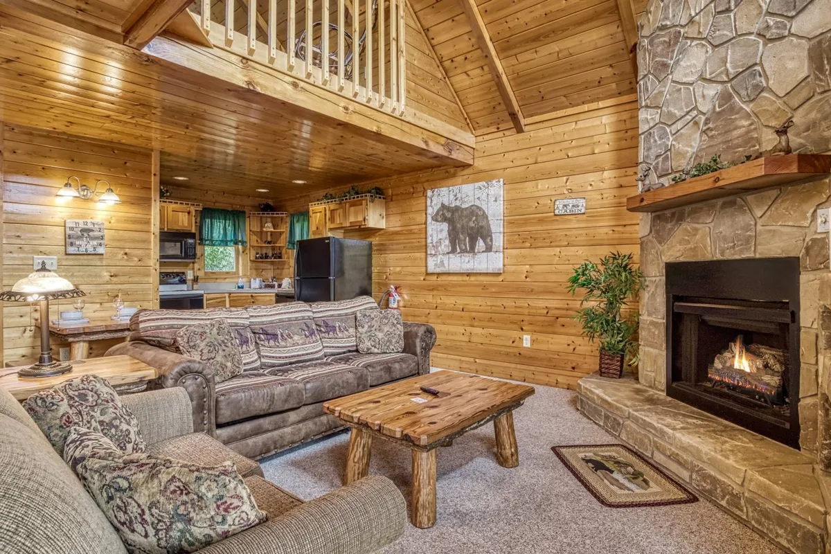 A cozy living area with a rustic stone fireplace, wooden coffee table, inviting sofa adorned with patterned cushions, and bear-themed artwork. The space is designed for intimate gatherings and moments of relaxation.
