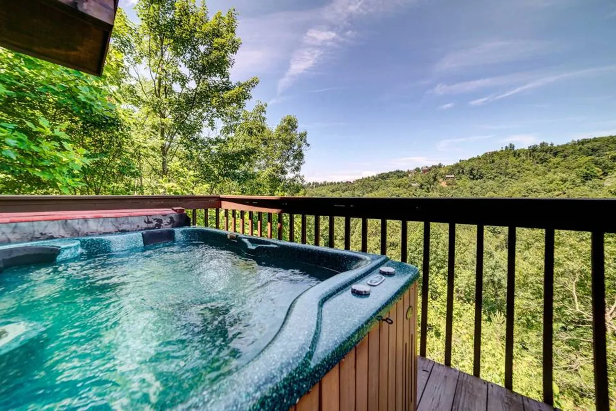 This image displays an outdoor hot tub set on a wooden deck, overlooking sweeping mountain views framed by lush trees. The atmosphere is serene, inviting guests to unwind and take in the natural surroundings after a day of adventure.