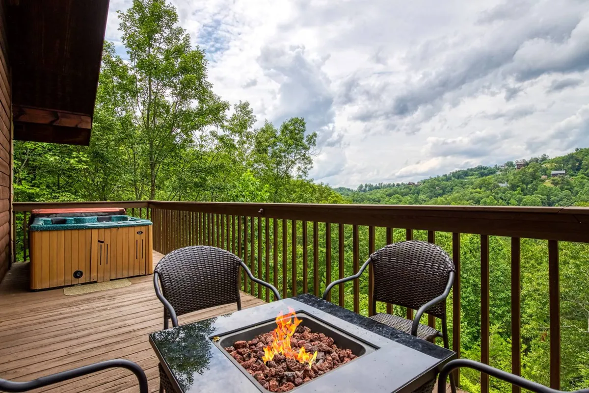 An exterior shot featuring both a hot tub and a fire pit, with a panoramic mountain backdrop and surrounding greenery. Guests are shown relaxing and socializing, illustrating the cozy, communal aspects of the resort.